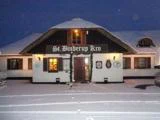 En snedækket traditionel bygning med stråtag og skiltet St. Binderup Kro over indgangen, varmt oplyste vinduer og spor i den snedækkede forgrund.