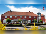 En rød murstensbygning med tegltag med navnet Tønderhus, der har udendørs siddepladser, velplejede buske og et dansk flag på en flagstang.