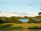 En malerisk udsigt over en sø omgivet af træer og marker, hvor man i det fjerne kan se en by og kirkespir under en klar himmel.