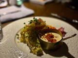 En anrettet gourmetret med en grøntsagsterrine, en lille gryde med cremet sauce toppet med stykker og pyntet med mikrogrønt på en hvid tekstureret tallerken.