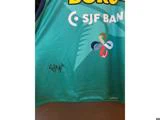 En turkis sportstrøje med en signatur med nummer 4, SJF Bank-logoet og et farverigt firkløver-emblem.