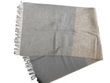 Et tofarvet tørklæde med frynsede kanter, med lysegrå og beige sektioner, lagt fladt på en hvid baggrund.