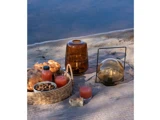 En picnic på et tæppe ved vandet med brød, nødder, juice i glas og flasker, en flettet kurv og to lanterner.