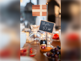 Et lille dansk flag og et skilt med teksten "Tillykke 37 år" står på et bord med en legetøjsvagt, glas og frugtskåle i festlige omgivelser.