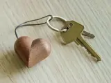 En metalnøglering med to nøgler og en hjerteformet nøglering i træ hviler på en lys træoverflade.