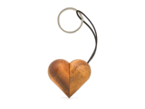 En hjerteformet nøglering af træ med metalring og sort snor, fotograferet på en hvid baggrund.