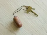 En messingnøgle fastgjort til en nøglering med en lille, brun, oval trænøglering, der ligger på en lys træoverflade.