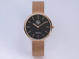 Et armbåndsur med mesh-rem i rosaguld med sort urskive, minimalistiske timemarkeringer og tekst i safirglas på urskiven mod en almindelig lys baggrund.