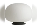 En moderne bordlampe med en stor, afrundet hvid lampeskærm og en lille, cirkulær sort fod på en ensfarvet hvid baggrund.