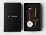 En sort Karlsson-urkasse med et armbåndsur med guldkant og en ekstra brun læderrem udstillet side om side.