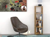 Et moderne værelse med en brun drejestol, en høj træreol med bøger og en lampe, et blåt tæppe og abstrakt kunst, der hænger på en hvid væg.