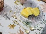 Tre skiver ananas på et glasfad formet som en ananas, med to ananasformede guldskeer på en blomstret dug.