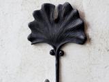 En sort metalknage formet som et ginkgoblad, monteret på en lys væg.