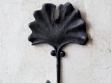 En sort metalknage formet som et ginkgoblad, monteret på en lys væg.