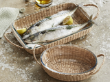 To hele rå fisk med citronbåde og dild i et flettet kurvfad ved siden af en tom mindre matchende kurv på en rustik overflade.