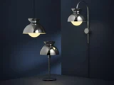 Tre moderne kromlamper – en pendel, en bordlampe og en væglampe – udstråler varmt lys på en mørkeblå baggrund og fremhæver de slanke, reflekterende metaldesign.