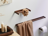 En badeværelsesscene med brune håndklædestænger i træ, der holder et beige håndklæde og en scrunchie, en toiletpapirrulle og toiletflasker på en bordplade af sten.