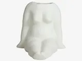 En hvid keramikvase formet som en stiliseret siddende nøgen kvindetorso uden hoved, hænder eller fødder og med minimale detaljer.