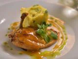 Anrettet stegt kyllingebryst med brun sauce, serveret med en firkantet skefuld kartoffelmos og pyntet med friske krydderurter og grøn oliedrys.