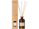 En brun glasflaske med etiketten ALTUM Meadow med sivdiffusorpinde ved siden af den høje papemballage, begge med Honey & Lemon-duft.