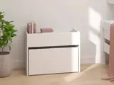 En hvid, moderne opbevaringskasse rummer tre bøger og en rektangulær genstand og står ved siden af en grøn potteplante på et lyst trægulv i et lyst, minimalistisk rum.