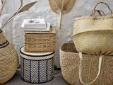 Flettede kurve og kasser i naturlige toner, med stablede bøger og dekorative tørrede palmeblade, arrangeret mod en hvid struktureret væg.