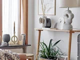 Minimalistisk stue med et konsolbord i træ, moderne indretning, planter, abstrakt kunst og naturligt lys fra et nærliggende vindue.