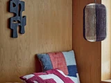 Et hyggeligt hjørne med en trævæg, en moderne sort vægskulptur, en patchwork-pude og en hængende stoflampeskærm.