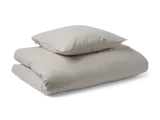 En foldet lys beige dyne og en matchende pude stablet pænt oven på hinanden mod en ensfarvet baggrund.