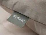Et nærbillede af et stofmærke mærket FLEXA® syet på beigefarvet sengetøj eller en pude.