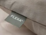 Nærbillede af en pude i beige stof med et grønt mærke med FLEXA® i hvid tekst.