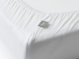 Nærbillede af et hvidt lagen med et synligt FLEXA-mærke, der pænt dækker hjørnet af en madras.