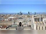 En panoramaudsigt over Milano, der viser Galleria Vittorio Emanuele II, Duomo di Milano og den moderne bys skyline under en klar blå himmel.