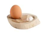 Et brunt æg og en lille bunke salt ligger på et rundt serveringsfad af træ med en udskåret fordybning til hver genstand på en hvid baggrund.