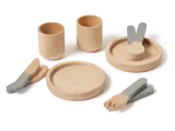 Et legetøjssæt i træ med to kopper, to tallerkener, bestik og en tang, alt sammen malet i naturtræ og grå farver, pænt arrangeret på en hvid overflade.