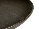 Nærbillede af kanten på en mørk, struktureret keramiktallerken med en glat, let skinnende overflade og en afrundet kant.