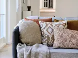 En hyggelig grå sofa med et strikket tæppe og fire pyntepuder i beige, brun og mønstret design i en lys, moderne stue.