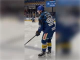 En ishockeyspiller i blåt udstyr med nummer 96 på trøjen glider hen over isen med en ishockeystav i hånden, mens en anden spiller og banden ses i baggrunden.