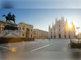 En solbeskinnet Piazza del Duomo i Milano med Milanos domkirke, en statue af en mand på hesteryg og et par mennesker, der går på pladsen.