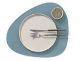 En rund, hvid tallerken med gaffel og kniv ovenpå, ved siden af en lille kop, alt sammen placeret på en blå, uregelmæssig dækkeserviet.
