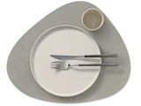 Minimalistisk borddækning med en rund tallerken, gaffel og kniv på kryds og tværs, en lille kop, alt sammen på en uregelmæssigt formet grå dækkeserviet.