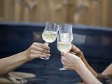 Tre hænder klirrer med vinglas fyldt med hvidvin over mørkt vand, muligvis mens de slapper af i et spabad eller en pool.