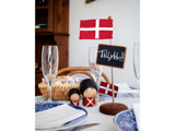 En borddækning med dansk tema med flag, soldaterfigurer i træ, en kurv med brød, vinglas og et kridttavleskilt med teksten Tillykke! omgivet af blå og hvide tallerkener.