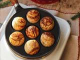 En pande med syv runde, gyldenbrune danske aebleskiver hviler på en hvid overflade med festlig udsmykning i nærheden.