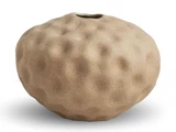Rund, beige keramikvase med fordybninger og en lille åbning øverst, set på en hvid baggrund.