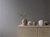 Et beige skab med strukturerede vaser og dekorative genstande i neutrale farver står op ad en ensfarvet grå væg.