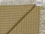 Nærbillede af et vævet stof i sennepsgult og hvidt med zigzagmønster og frynsede kanter. Stoffet er foldet diagonalt, så man kan se for- og bagside.