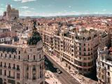 Luftfoto af Madrid med den udsmykkede Metropolis-bygning, travle gader, klassisk arkitektur og fjerne bjerge under en klar himmel.