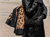 Person i sort læderfrakke og handsker, der holder et Rhanders-tørklæde med leopardprint og en quiltet sort taske udendørs.