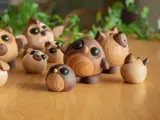 En gruppe søde, runde trædyrfigurer med store sorte øjne er arrangeret på en træoverflade med grønne planter sløret i baggrunden.